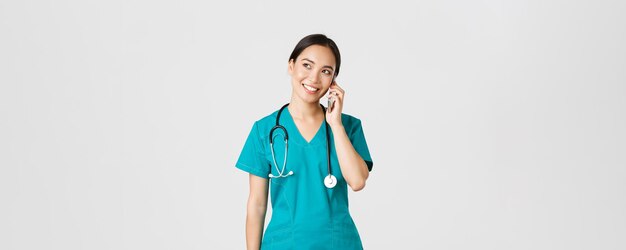 Covid-19, operatori sanitari e prevenzione del concetto di virus. Dottoressa asiatica abbastanza sorridente, medico in camice che ha conversazione, parla al telefono e sembra sognante nell'angolo in alto a sinistra.