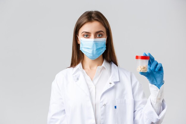 Covid-19, prevenzione del virus, operatori sanitari e concetto di quarantena. Dottore in camice e maschera medica, mostrando un contenitore con pillole, raccomanda vitamine o antibiotici