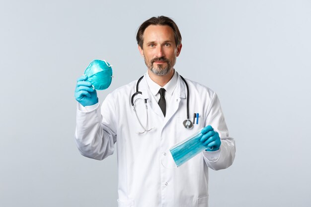 Covid-19, prevenzione del virus, operatori sanitari e concetto di vaccinazione. Il dottore in guanti e camice bianco spiega la differenza tra respiratore medico e maschera, sorridente amichevole