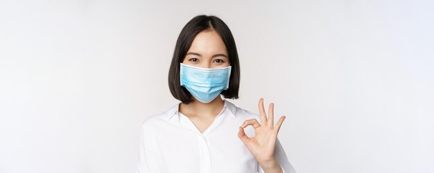 Covid e concetto di salute ritratto di donna asiatica che indossa una maschera medica e mostra un segno giusto sta