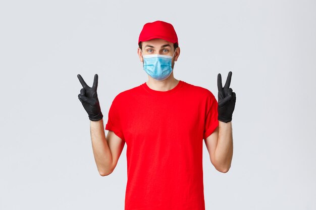 Covid selfquarantine shopping online e concetto di spedizione simpatico ragazzo delle consegne in uniforme rossa maschera facciale...