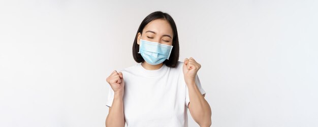 Covid19 concetto sanitario e medico Donna asiatica entusiasta in maschera medica che balla e celebra la vittoria raggiungere l'obiettivo in piedi su sfondo bianco