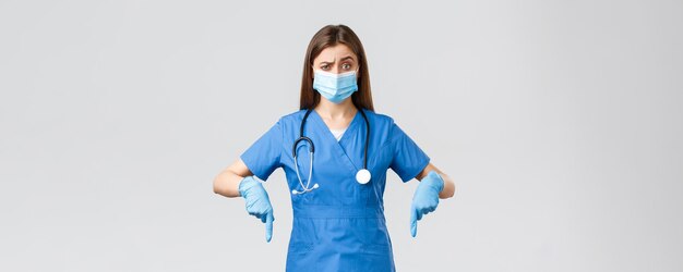 Covid19 prevenzione del virus operatori sanitari sanitari e concetto di quarantena Infermiera o dottoressa scettica e insicura in blu strofina i dispositivi di protezione individuale puntando il dito verso il basso incerti