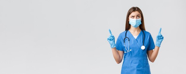 Covid19 prevenzione del virus operatori sanitari sanitari e concetto di quarantena Infermiera scettica e sospettosa in blu scrub stetoscopio e maschera medica che punta il dito verso l'alto