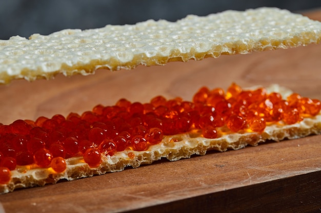 Cracker con caviale rosso su una tavola di legno, primi piani.