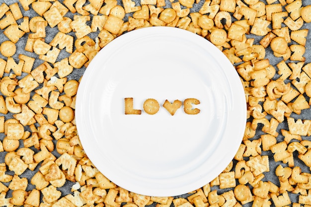 Cracker di alfabeto sparsi e amore di parola scritto con i cracker su un piatto bianco.