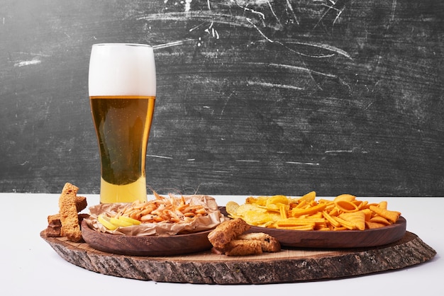 Cracker e patatine fritte con un bicchiere di birra su bianco.