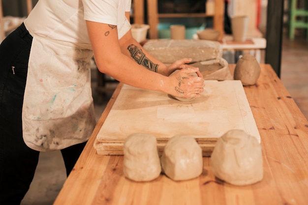 Craftswoman che impasta l&#39;argilla sul bordo di legno sopra la tavola