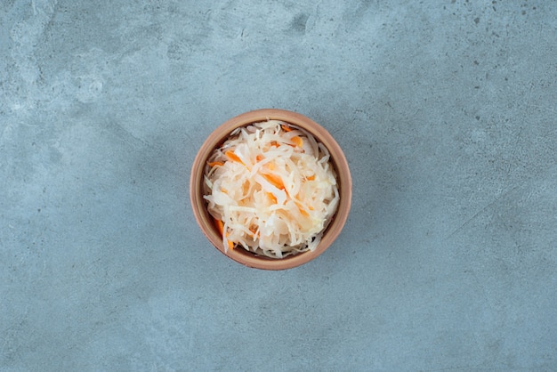 Crauti fermentati con carote in una ciotola di argilla, sul tavolo blu.