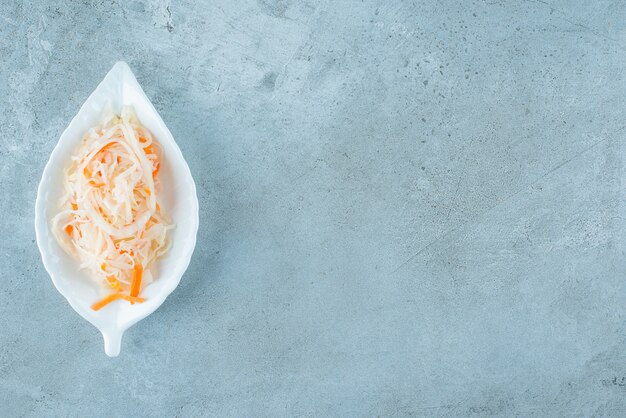 Crauti fermentati con carote ione un piatto da portata, sul tavolo blu.