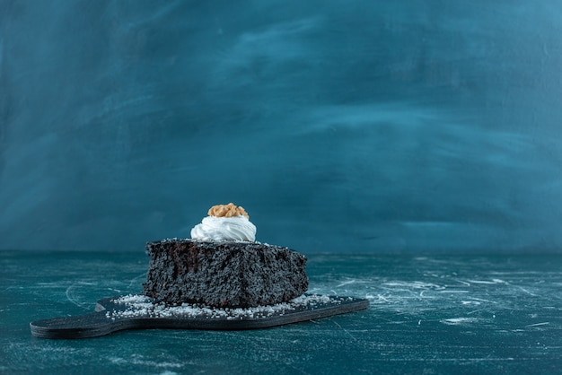 Crema e noci topping su una fetta di torta al cioccolato su una piccola tavola sul blu.