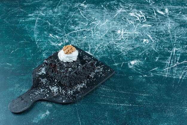 Crema e noci topping su una fetta di torta al cioccolato su una piccola tavola sul blu.