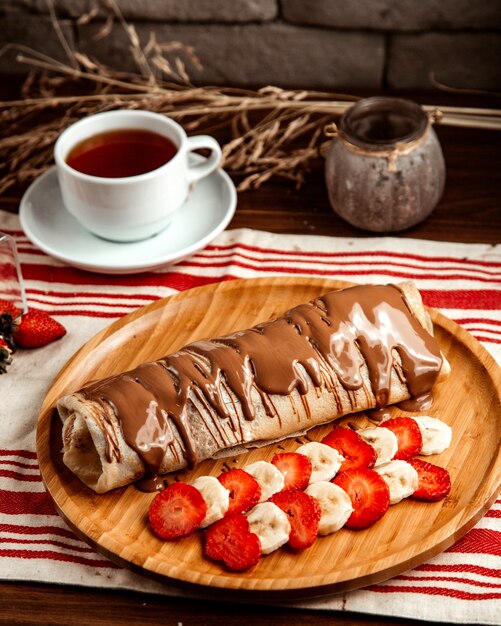 Crepe con vista laterale del tè al cioccolato della banana della fragola della frutta