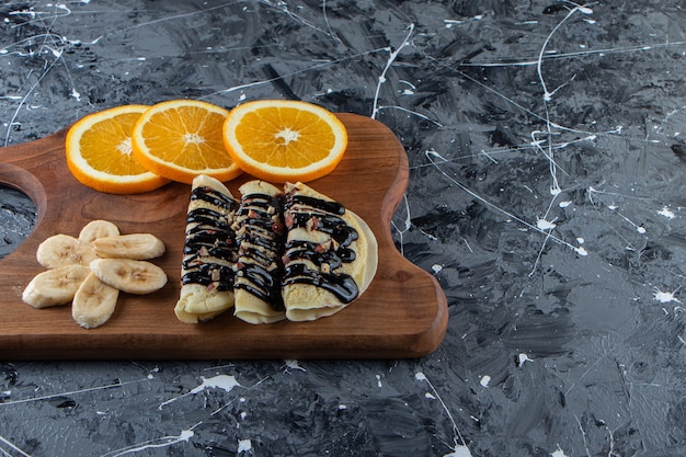 Crepes fatte in casa con cioccolato, banana a fette e arancia su tavola di legno.