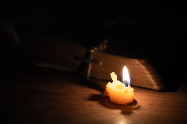 Croce con la Bibbia e la candela su un vecchio tavolo di legno di quercia.