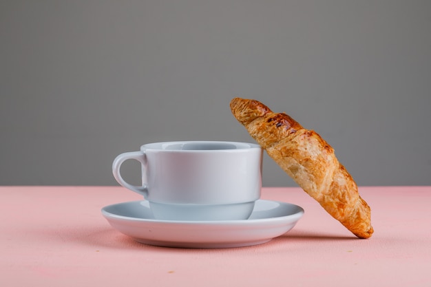 Croissant con la tazza di tè sulla tavola rosa e grigia, vista laterale.