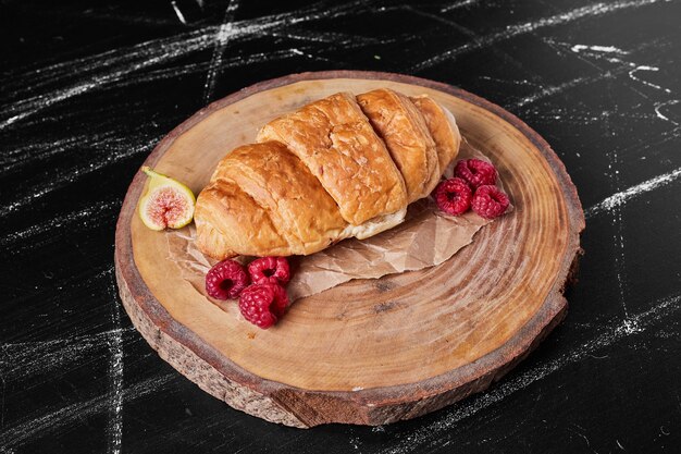 Croissant con lamponi sul piatto di legno.