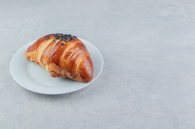 Croissant fresco decorato con cioccolato a goccia su piatto bianco.