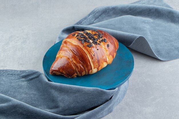 Croissant fresco decorato con gocce di cioccolato su tavola blu.