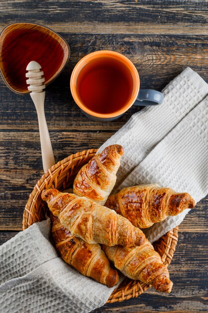 Croissant in un cestino con miele, mestolo, vista superiore del tè su un tavolo di legno