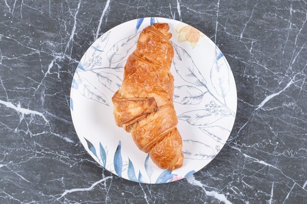 Croissant normale nel piatto, sulla superficie di marmo