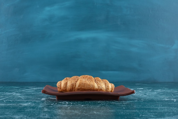 Croissant su un piatto marrone, sul tavolo blu.