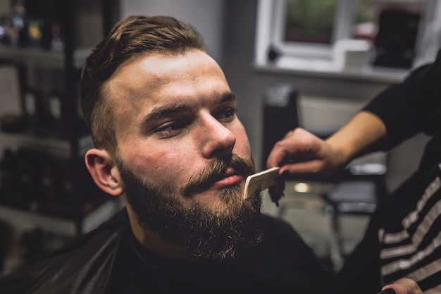 Crop barbiere che pettina la barba dell&#39;uomo