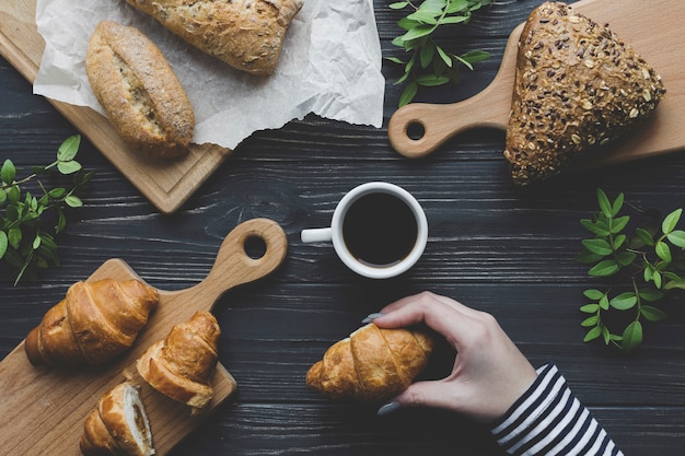 Crop mano che tiene croissant vicino al caffè