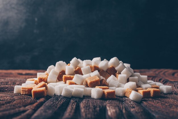 Cubi dello zucchero bianco e marrone di vista laterale sulla tavola scura e di legno. orizzontale