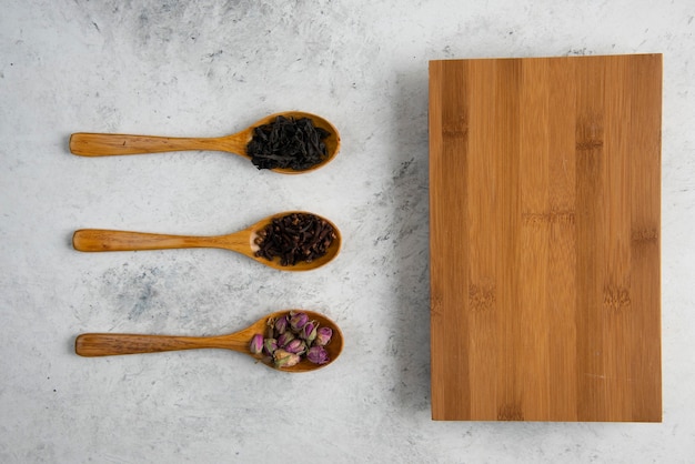 Cucchiai di legno con rose essiccate, tè sfusi e chiodi di garofano.