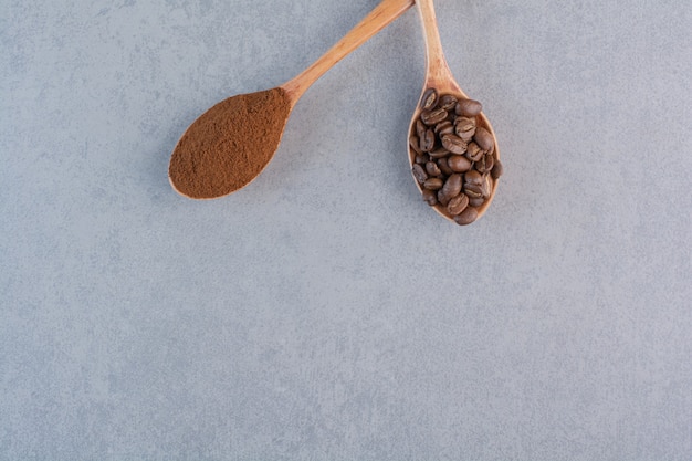 Cucchiai di legno di caffè macinato e tostato su fondo di pietra.