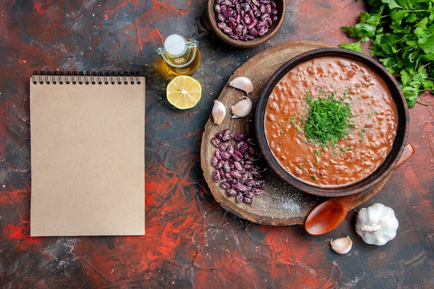 Cucchiaio di aglio di fagioli di sapone di pomodoro sul tagliere di legno e bottiglia di olio verde limone accanto al taccuino