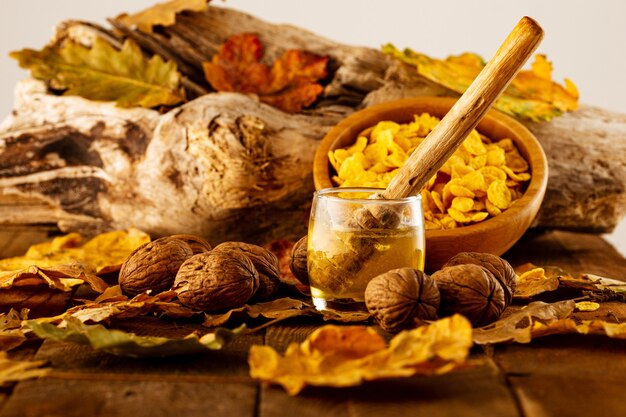 Cucchiaio di legno all'interno di un barattolo di miele con noci e una ciotola di cereali su foglie autunnali sfondo sfocato