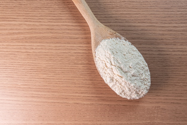 Cucchiaio di legno con farina di frumento su tavola di legno