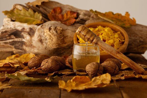 Cucchiaio di legno con miele gocciolante su un barattolo, noci e cereali su un muro sfocato di foglie autunnali