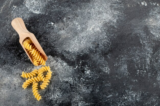 Cucchiaio di legno di fusilli crudi sulla superficie in marmo