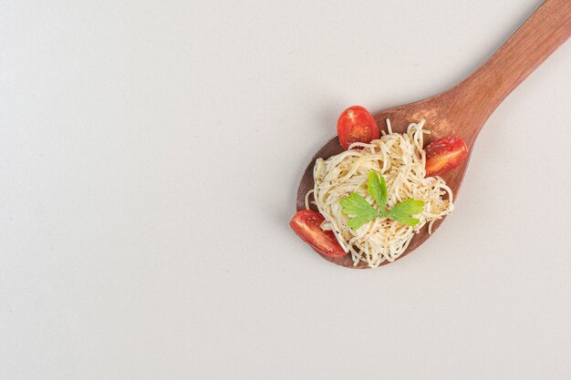 Cucchiaio di spaghetti con fette di pomodoro e prezzemolo su superficie bianca