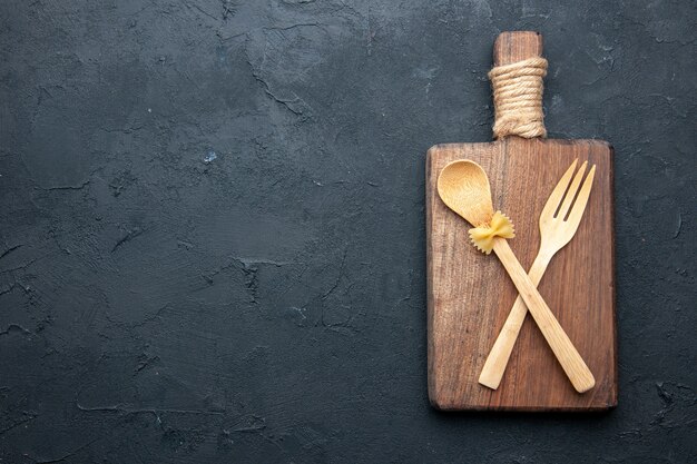 Cucchiaio e forchetta di legno incrociati vista superiore sul bordo di legno del servizio sul posto della copia della tavola nera