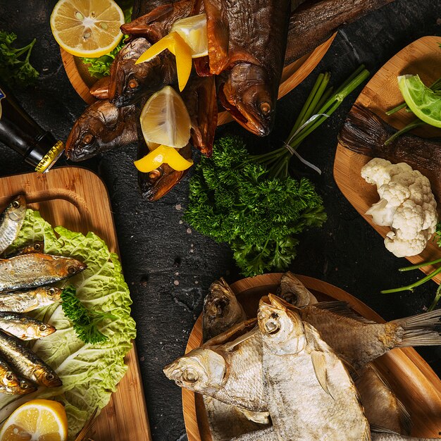 Cucina mediterranea, pesce di aringa affumicato servito con cipolla verde, limone, pomodorini, spezie, pane e salsa Tahini su scuro. Vista dall&#39;alto con close-up