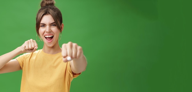 Cucina ribelle donna in maglietta gialla con i denti a fessura che tira il pugno verso la telecamera come se mostrasse un combattimento