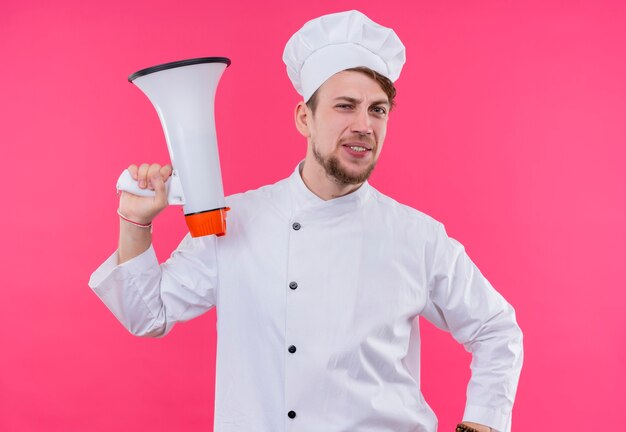 Cucinare guardando il sorriso della fotocamera sul viso con altoparlante in piedi sopra la parete rosa