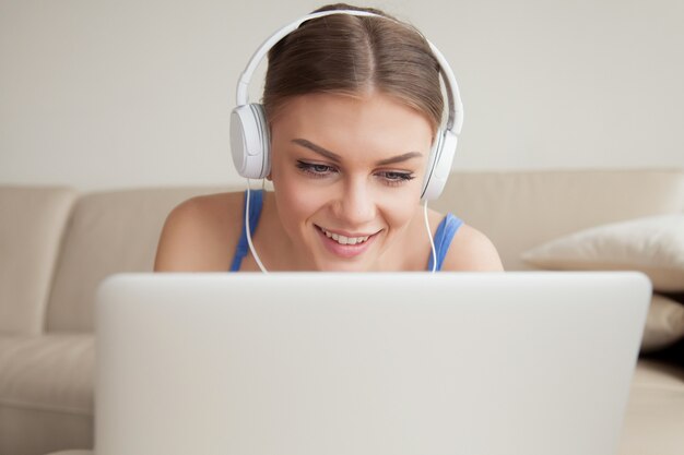 Cuffie d&#39;uso sorridenti della giovane donna facendo uso del computer portatile, colpo in testa