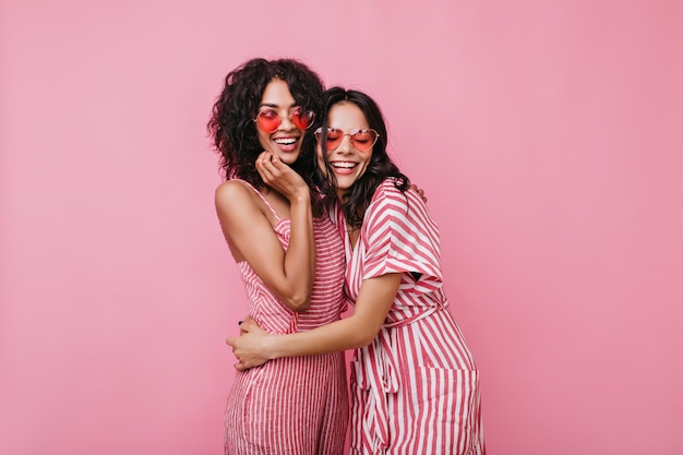 Cugini in capelli ricci scuri di ottimo umore in posa per il ritratto. Le ragazze in abiti rosa si divertono.