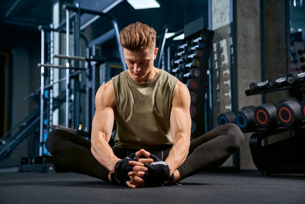 Culturista che fa allungamento della farfalla sul pavimento in palestra.