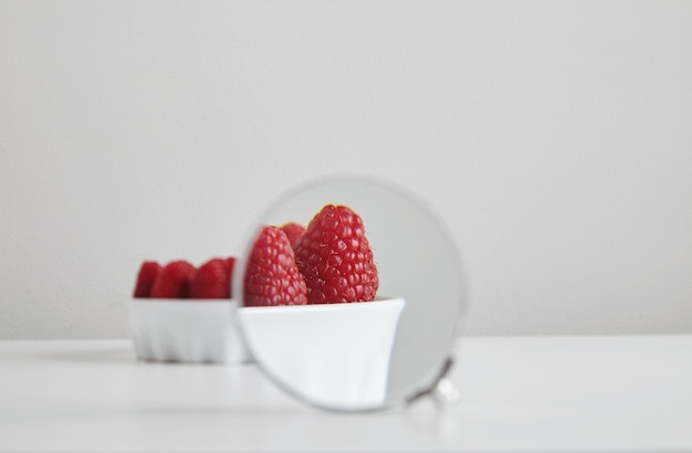 Cumulo di lampone maturo superfood organico nel concetto di ciotola di ceramica per mangiare sano e nutrizione isolato sul tavolo bianco, ingrandito tramite lente di ingrandimento binoculare per vedere i dettagli