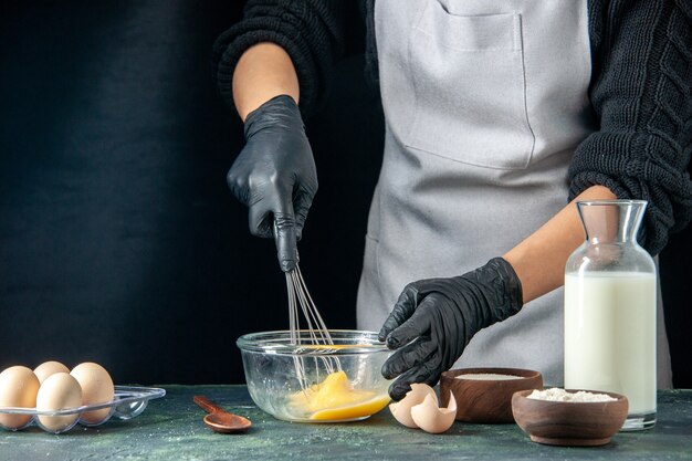 Cuoca di vista frontale che mescola le uova per l'impasto su torta di pasticceria scura torta lavoratore cucina lavoro hotcake