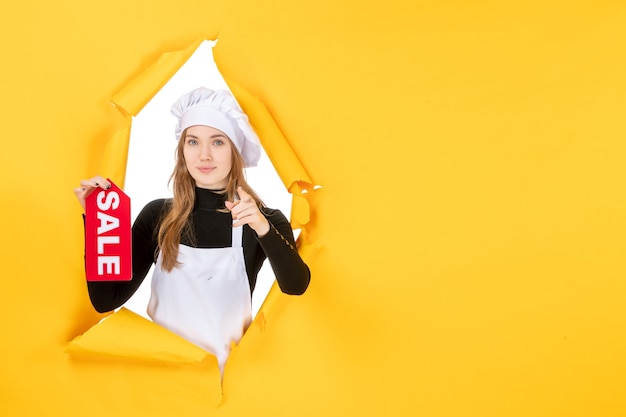 Cuoca di vista frontale che tiene la vendita rossa che scrive sul colore giallo lavoro cucina cucina cibo foto