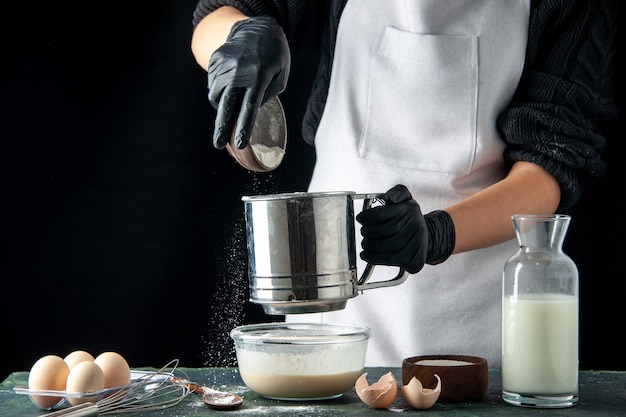 Cuoca di vista frontale che versa farina nelle uova sulla torta di pasticceria scura torta di pasticceria lavoro pasta lavoratore