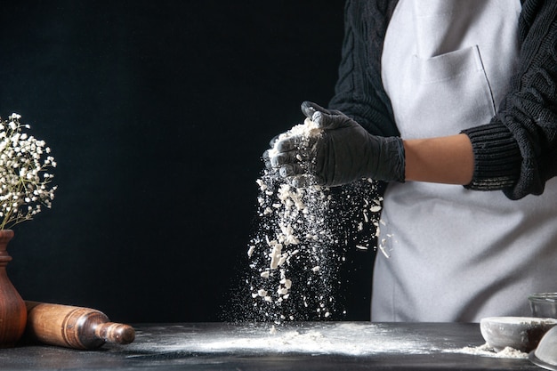 Cuoca di vista frontale che versa farina sul tavolo per l'impasto su pasta scura uovo cucina lavoro panetteria hotcake pasticceria cucina