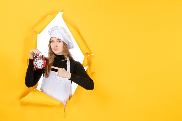 Cuoca di vista frontale in berretto da cuoco bianco che tiene l'orologio sul colore giallo lavoro emozione cibo cucina cucina sole